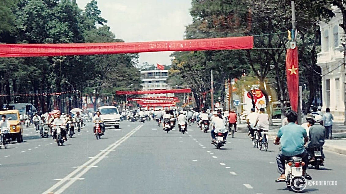 This photo, taken on April 30, 1995, from a taxi on my way to the airport in Ho Chi Minh City, captures the wide boulevards in Saigon, a former French colonial city which mirrors Paris in many ways. The photo was likely taken on Nguyễn Thị Minh Khai Street, a major road leading toward Tan Son Nhat Airport, decorated for the 20th anniversary celebrations. The main banner reads “Welcome to 20 Years of National Reunification Day, April 30, 1975 – April 30, 1995,” 
