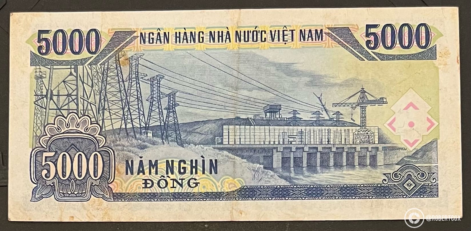 5,000 Vietnamese đồng banknote issued by the State Bank of Vietnam (Ngân Hàng Nhà Nước Việt Nam). The note features an illustration of the Trị An Hydropower Plant, a major hydroelectric dam located in Đồng Nai Province, southeast of Ho Chi Minh City. The image on the banknote shows the dam structure with its spillways, power lines, and transmission towers, symbolizing Vietnam’s industrial development and energy infrastructure under communist rule.